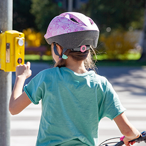 Child wearing bicycle helmet standing next to bicycle at intersection, pressing button to walk