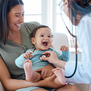 Woman holding smiling baby; healthcare provider listening to baby's chest with stethoscope