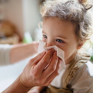 Adult wiping young child's nose with tissue