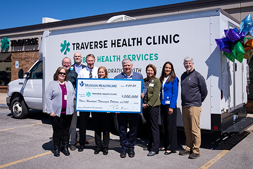 Representatives from Munson Healthcare and Traverse Health Clinic standing in front of the mobile medical unit with a large check